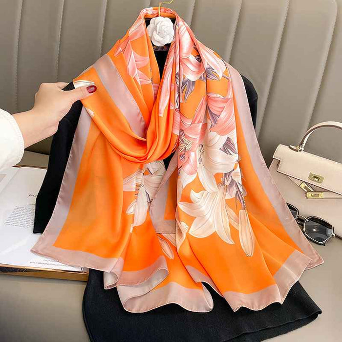 Vibrant orange silk-satin scarf featuring a large lily floral print and a mauve-grey bordered edge